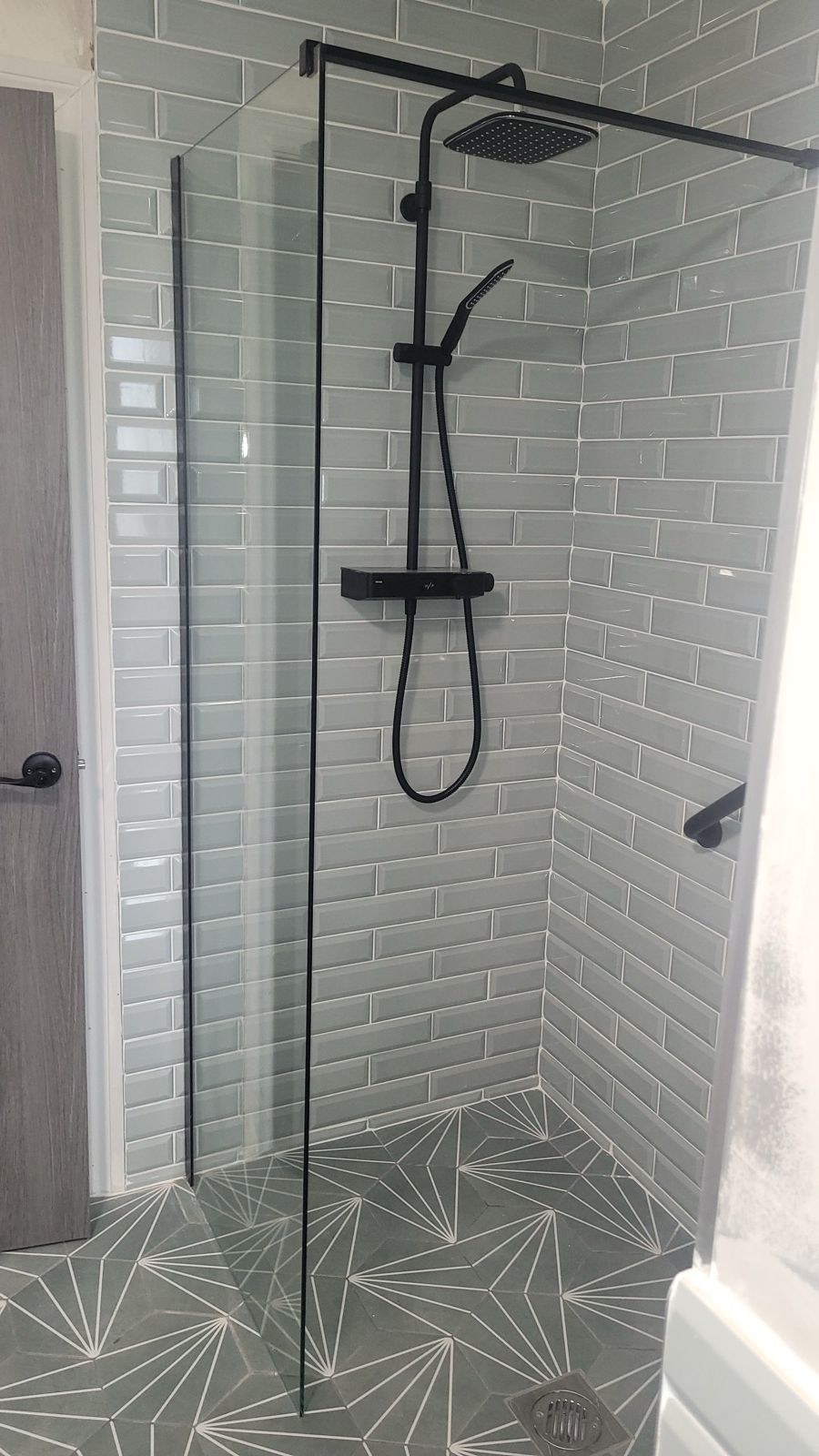 Sage metro-tiled shower with black fittings and geometric floor